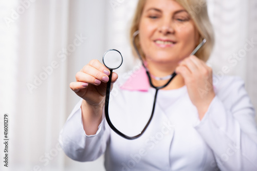 It's time for a check up in clinic, female doctor holds stethoscope stretched to camera. Health care concept with side white space