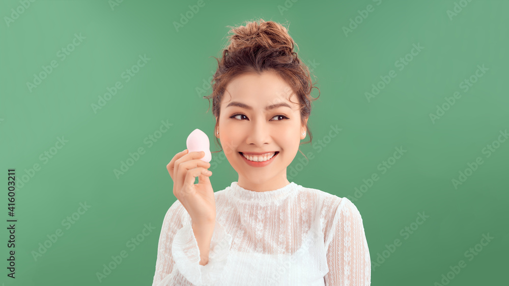 Woman applying foundation with beauty blender over green background Woman applying foundation with beauty blender over green background