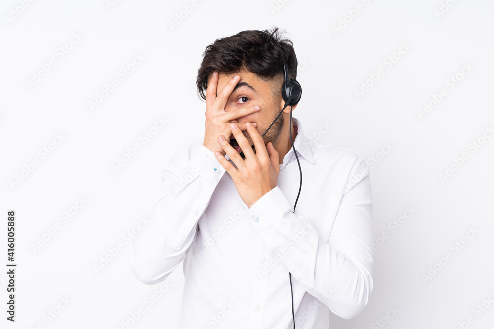 Telemarketer Arabian man working with a headset isolated on white background covering eyes and looking through fingers Telemarketer Arabian man working with a headset isolated on white background covering eyes and looking through fingers