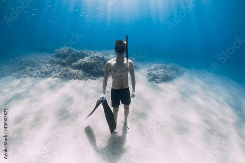 Sporty man freediver stay with fins on sandy bottom underwater in blue sea.
