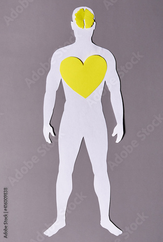 A paper silhouette of a man with a yellow brain and heart on a gray background.