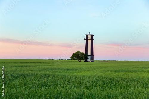 Lighthouse building. Old black and white lighthouse building stands on land in field at pink sunset in summer evening.