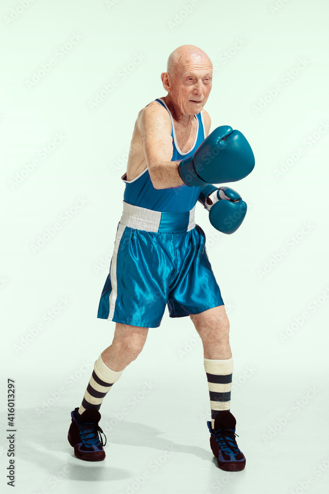 Punch. Senior man wearing sportwear boxing on studio background. Caucasian male model in great shape stays active and sportive. Concept of sport, activity, movement, wellbeing. Copyspace, ad.