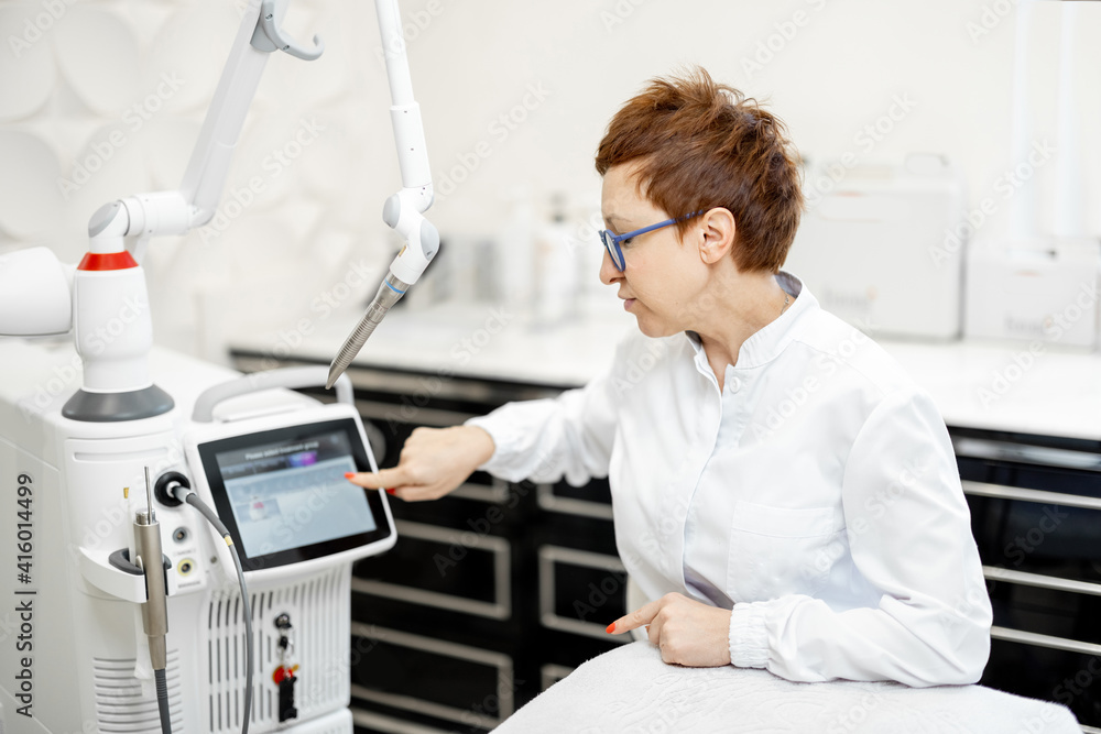 Cosmetologist near laser treatment device in beauty clinic. Anti-age, non-invasive, non-surgical laser facelift for natural-looking results concept. Cosmetologist near laser treatment device in beauty clinic. Anti-age, non-invasive, non-surgical laser facelift for natural-looking results concept.