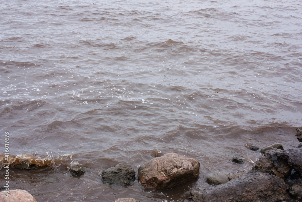 stones on the shore of a large pond, lake or sea, dark water, small ripples and waves stones on the shore of a large pond, lake or sea, dark water, small ripples and waves