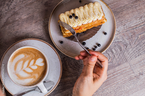 Mujer cortando milhoja con tenedor acompañada de un capucchino photo