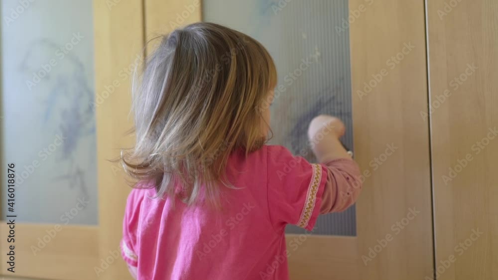 Curly cute little baby girl drawing with crayon color on the cupboard, focused smart preschool child enjoying creative art hobby activity at home, children development concept Curly cute little baby girl drawing with crayon color on the cupboard, focused smart preschool child enjoying creative art hobby activity at home, children development concept