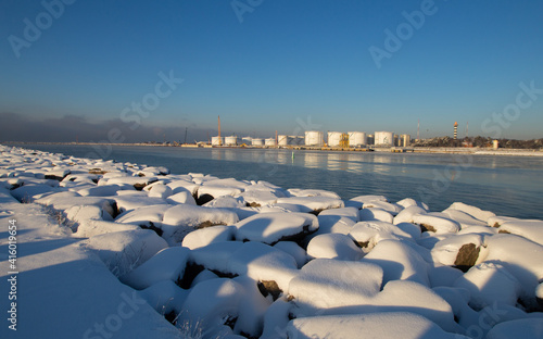 Curonian spit pier with protecting barrier rocks, industrial port docks covered by snow. Beautiful sunny weather and blue sky. Klaipeda Lithuania