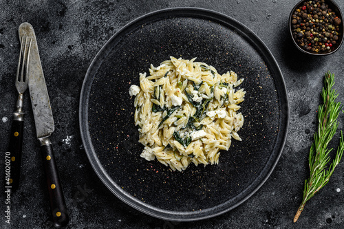 Homemade spinach orzo pasta on a plate. Black background. Top view