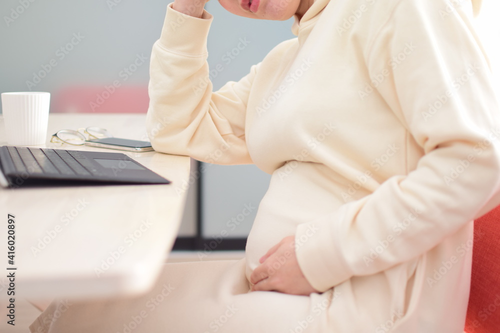 A pregnant woman in her twenties works from home using a laptop with fear of coronavirus and flu virus.She is working hard at home while feeling nauseous, headache and illness.