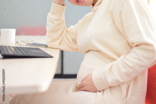 A pregnant woman in her twenties works from home using a laptop with fear of coronavirus and flu virus.She is working hard at home while feeling nauseous  headache and illness.