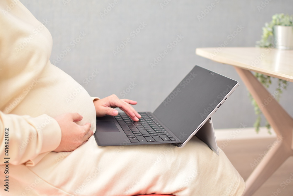 Naklejka premium A pregnant woman in her twenties works from home using a laptop with fear of coronavirus and flu virus.
