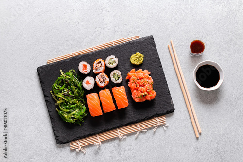 Sushi takeaway with sushi set, wakame salad, chopsticks and sauces on gray concrete background, top view
