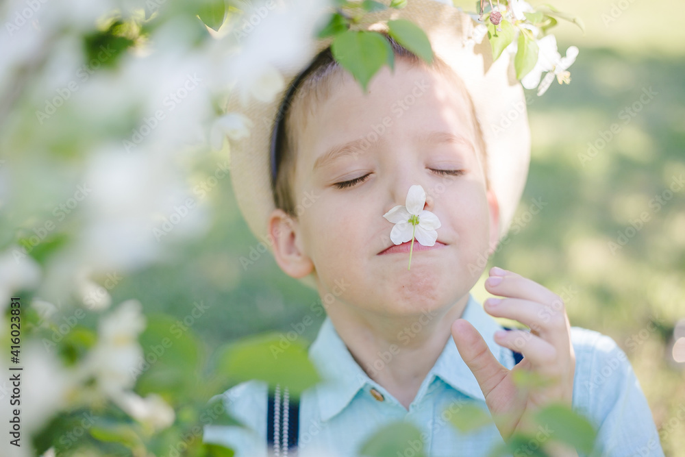 A child in a hat in a flowering garden sniffs a flower. A child in a hat in a flowering garden sniffs a flower.