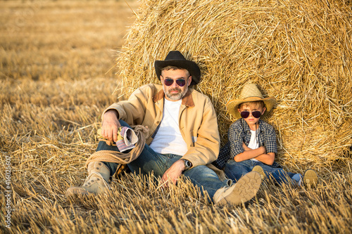 Father and son resting in the field wear hats, shirts and jeans. Son like as father concept
