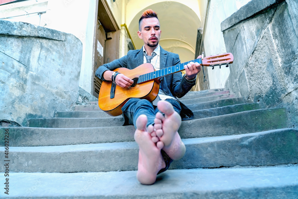 Male street musician playing guitar outdoors with bare feet in old European city. Art and music concept. Male street musician playing guitar outdoors with bare feet in old European city. Art and music concept.