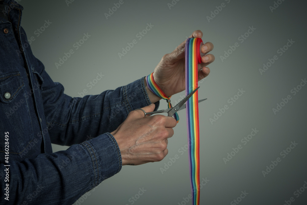 man hand with rainbow bracelet cutting a rainbow ribbon with scissors