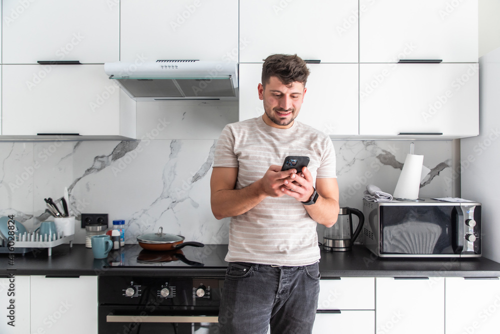 Handsome young man texting with his smartphone in kitchen