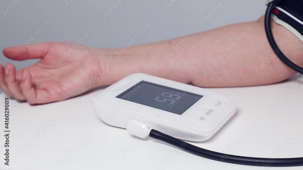 An adult or an elderly woman measures blood pressure with a measuring blood pressure with portable digital tonometer at home. An adult or an elderly woman measures blood pressure with a measuring blood pressure with portable digital tonometer at home.