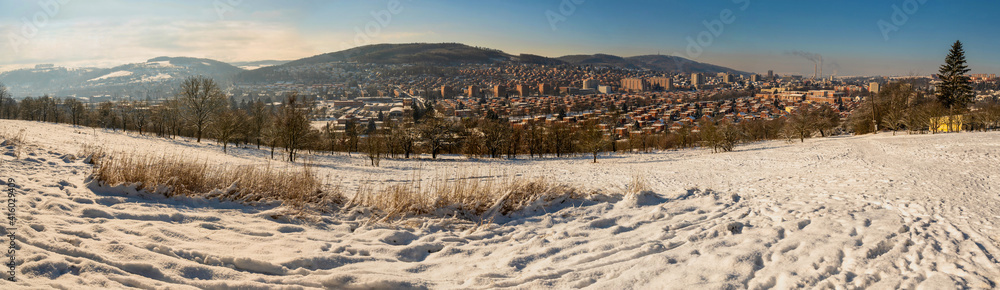 Panorama of city Zlin in valley between hills with typical red brick buildings from snowy meadow