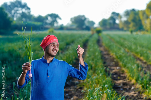 Young indian farmer holding onion crop in hand at agriculture field