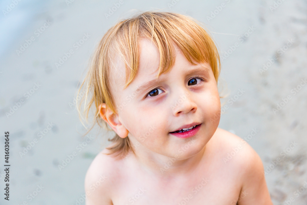 Close up portrait of a little toddler boy of three years old staying on a sandy sea beach. Child spending ocean vacation at the seaside. Close up portrait of a little toddler boy of three years old staying on a sandy sea beach. Child spending ocean vacation at the seaside.