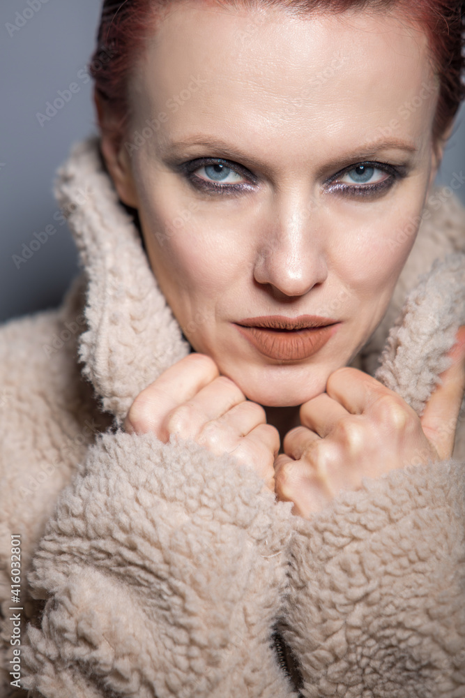 Beautiful red hair woman wearing artificial fur coat over grey background Beautiful red hair woman wearing artificial fur coat over grey background
