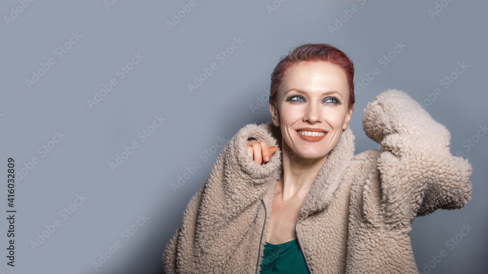 Beautiful red hair woman wearing artificial fur coat over grey background Beautiful red hair woman wearing artificial fur coat over grey background