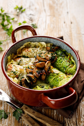 Traditional cabbage rolls stuffed with rice and mushrooms in an enamel dish on a wooden table, close up view