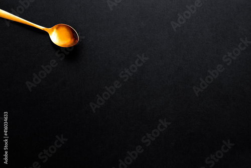 A gold colored soup spoon in one corner, isolated on black background with copy space.