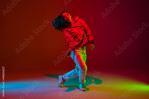 Freedom. Stylish sportive girl dancing hip-hop in stylish clothes on colorful background at dance hall in neon light. Youth culture, movement, style and fashion, action. Fashionable bright portrait.