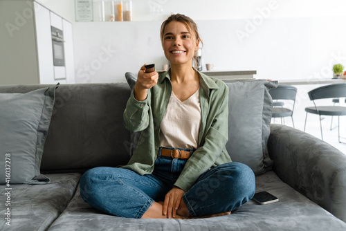 Happy nice woman watching TV with remote control while sitting on sofa