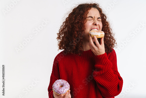 Fototapeta Excited ginger young woman grimacing while eating doughnuts