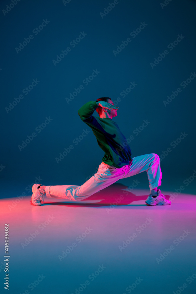 Flexible. Stylish sportive boy dancing hip-hop in stylish clothes on colorful background at dance hall in neon light. Youth culture, movement, style and fashion, action. Fashionable bright portrait.