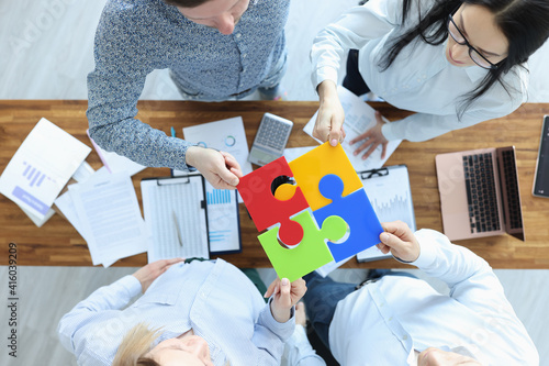 Group of business people are sitting at table and putting together colorful puzzle top view. photo