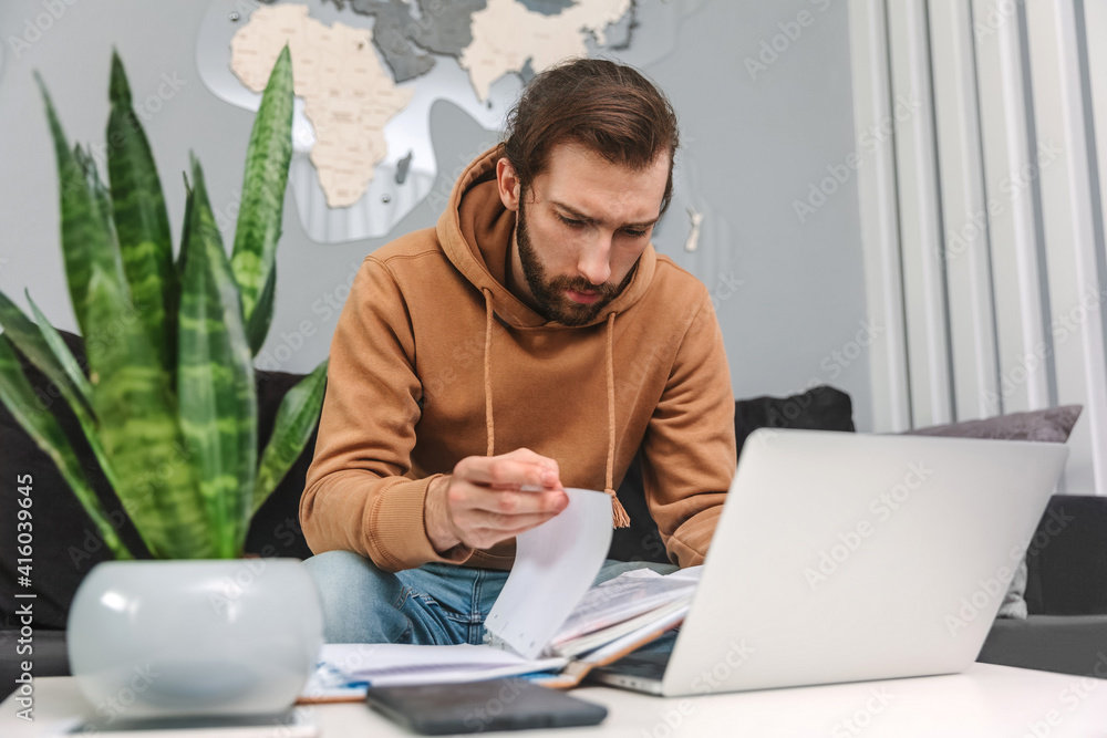 Concentrated man working at home using laptop and leafing through notepad Concentrated man working at home using laptop and leafing through notepad