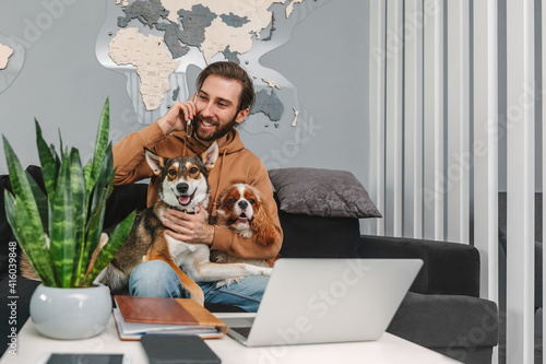 Photography Young man talking on mobile phone while sitting on sofa and hugging dogs