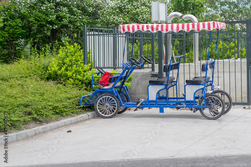 A multi-seat tandem bike with a red and white striped canopy is rented in the parking lot. Budapest, Hungary.
