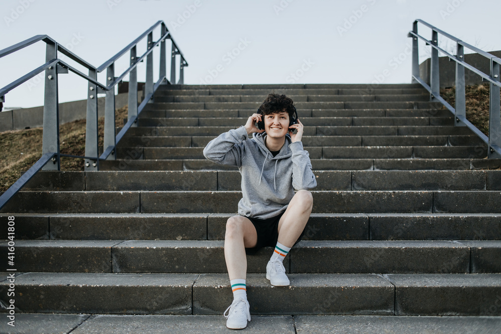 Junger Mensch sitzt auf Treppe und hört Musik mit Kopfhörern sportlich gekleidet Junger Mensch sitzt auf Treppe und hört Musik mit Kopfhörern sportlich gekleidet