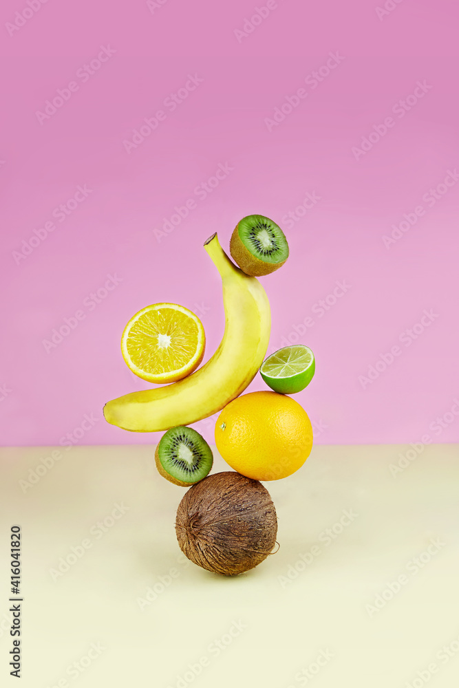 Balancing fruits: orange, coconut, banana, kiwi and lime on a colored paper  background. Equilibrium floating food balance. Photos | Adobe Stock