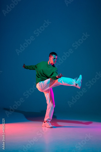 Modern. Stylish sportive boy dancing hip-hop in stylish clothes on colorful background at dance hall in neon light. Youth culture, movement, style and fashion, action. Fashionable bright portrait. © master1305