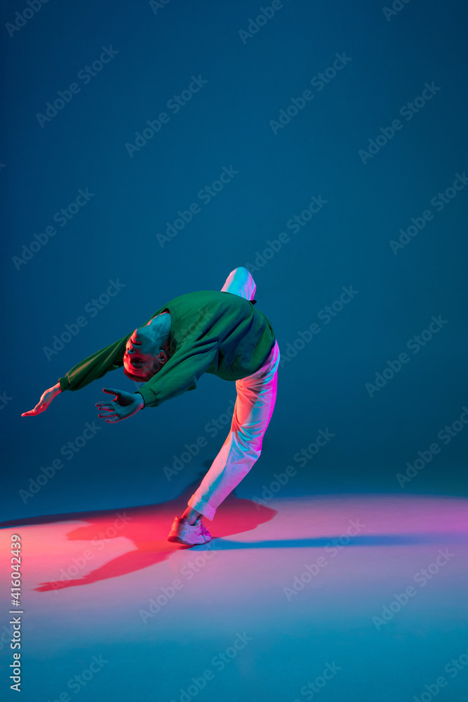 Fashion. Stylish sportive boy dancing hip-hop in stylish clothes on colorful background at dance hall in neon light. Youth culture, movement, style and fashion, action. Fashionable bright portrait.