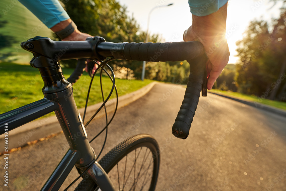 Obraz premium Close up shot of hands on handlebar. Professional male bicycle racer riding his road bike in the park at sunset