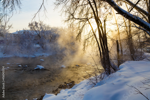 The rays of the sun break through the winter branches of the trees on the bank of the river with fog. the bitter cold of minus 30 degrees Celsius.