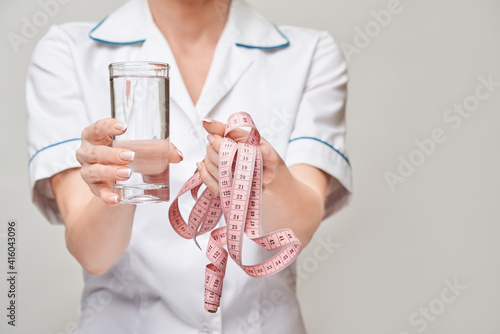 Healthy eating or lifestyle concept - female woman doctor holding and a glass of clear fresh water and measure tape
