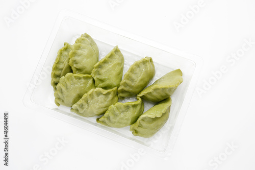 Top view of green pierogi, dumplings on a plastic, transparent food tray, isolated on white.