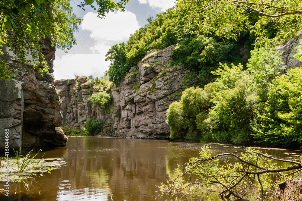 Canyon between which flows a river against the blue sky and green trees