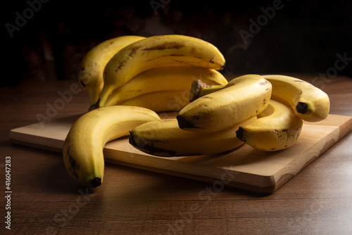 Bananas put on wood on a table, dark abstract background, directional light, selective focus.