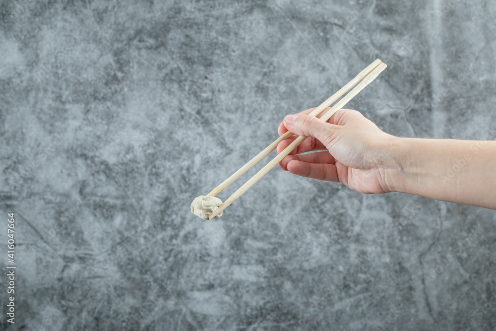 Hand holding a chopstick with a dumpling Hand holding a chopstick with a dumpling