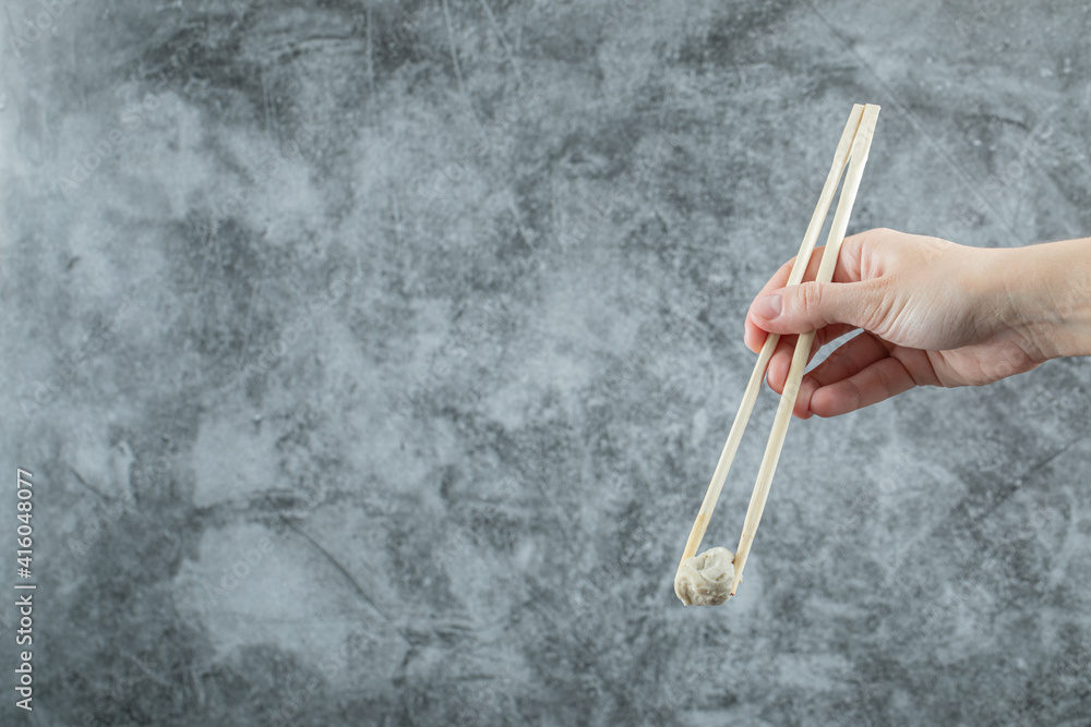 Hand holding a chopstick with a dumpling Hand holding a chopstick with a dumpling